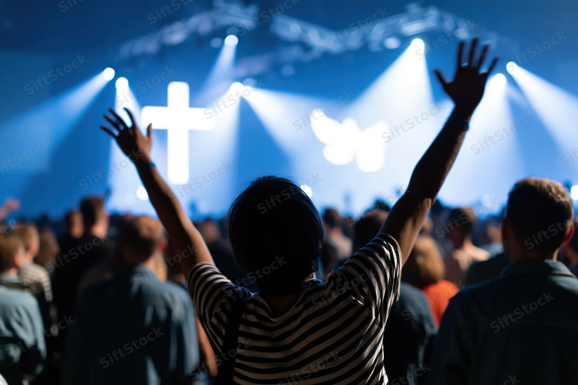 Woman with arms raised in worship facing a lit cross on stage in a modern church congregation