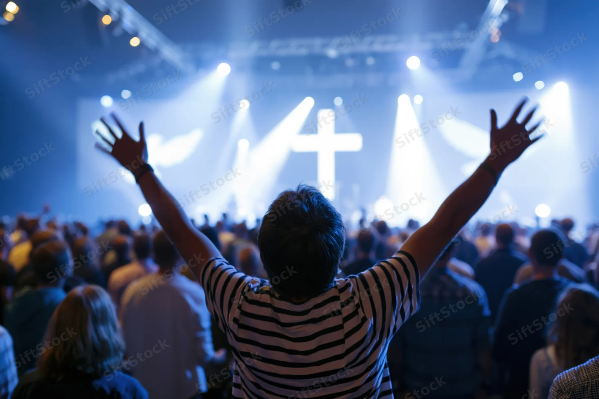 Man with arms raised facing a lit cross on stage during a church service