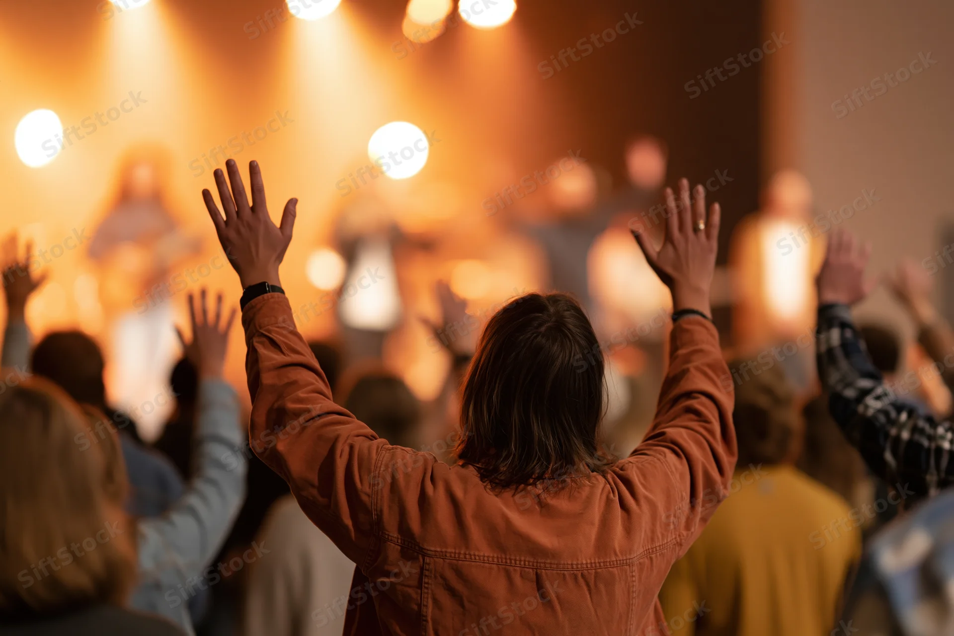 Woman with arms raised in worship facing a stage with lights and a band during a church service