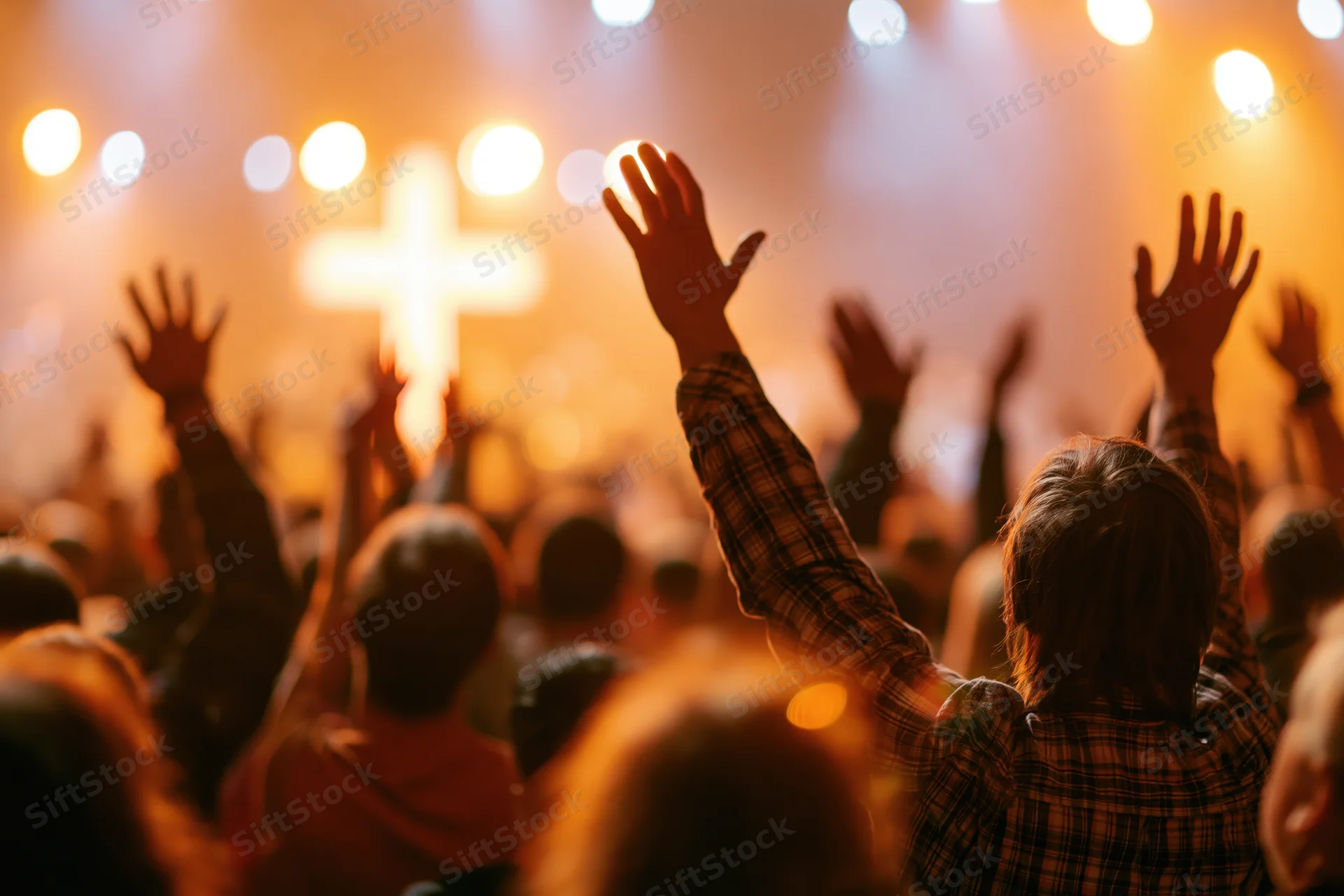 Congregation raising hands in worship during a church service with illuminated cross on stage
