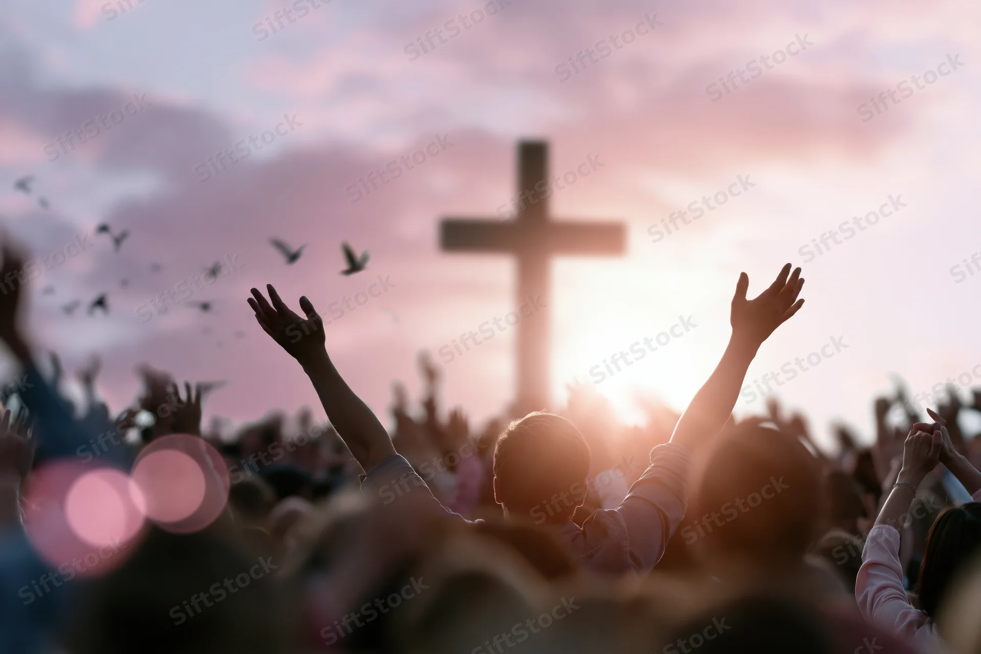 Silhouetted worshippers raising hands toward a large cross at sunset