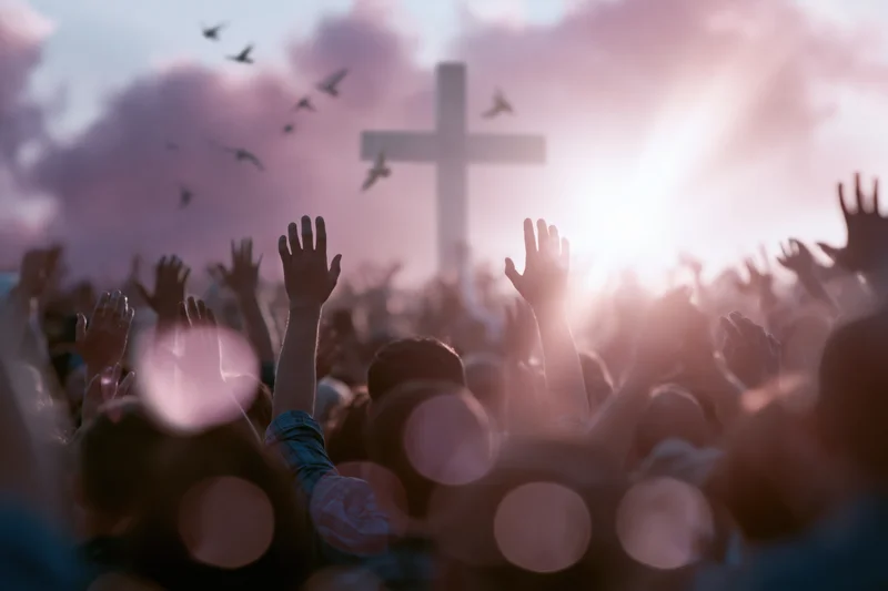 Crowd of worshippers raising hands toward a large cross at sunset