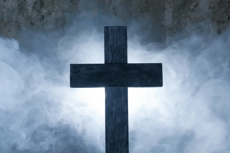 Dark wooden christian cross silhouetted against swirling smoke in a cemetery setting