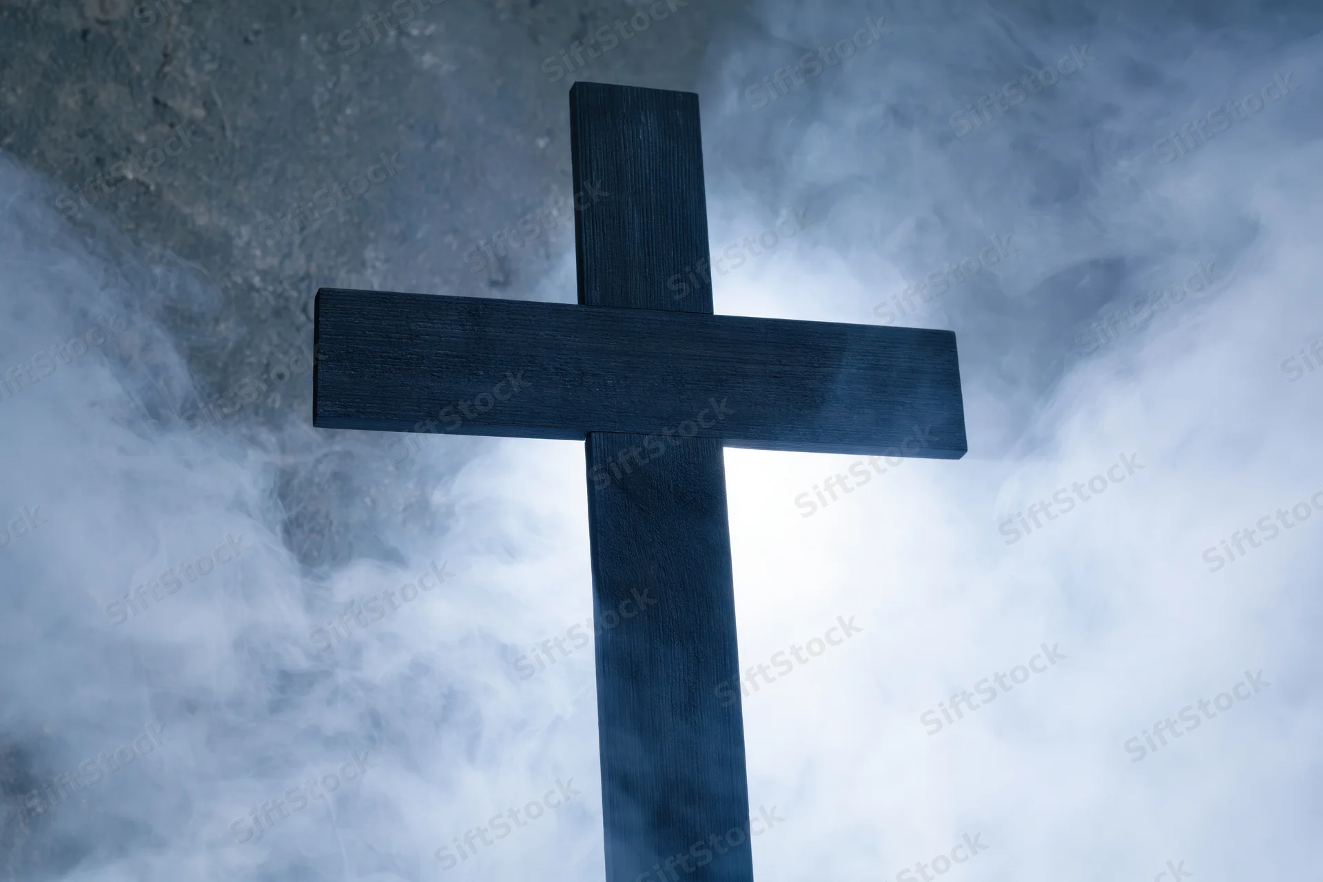 Dark wooden christian cross silhouetted against swirling smoke and mist