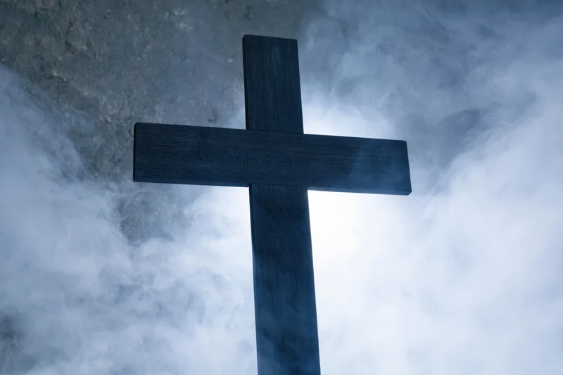 Dark wooden christian cross silhouetted against swirling smoke and mist