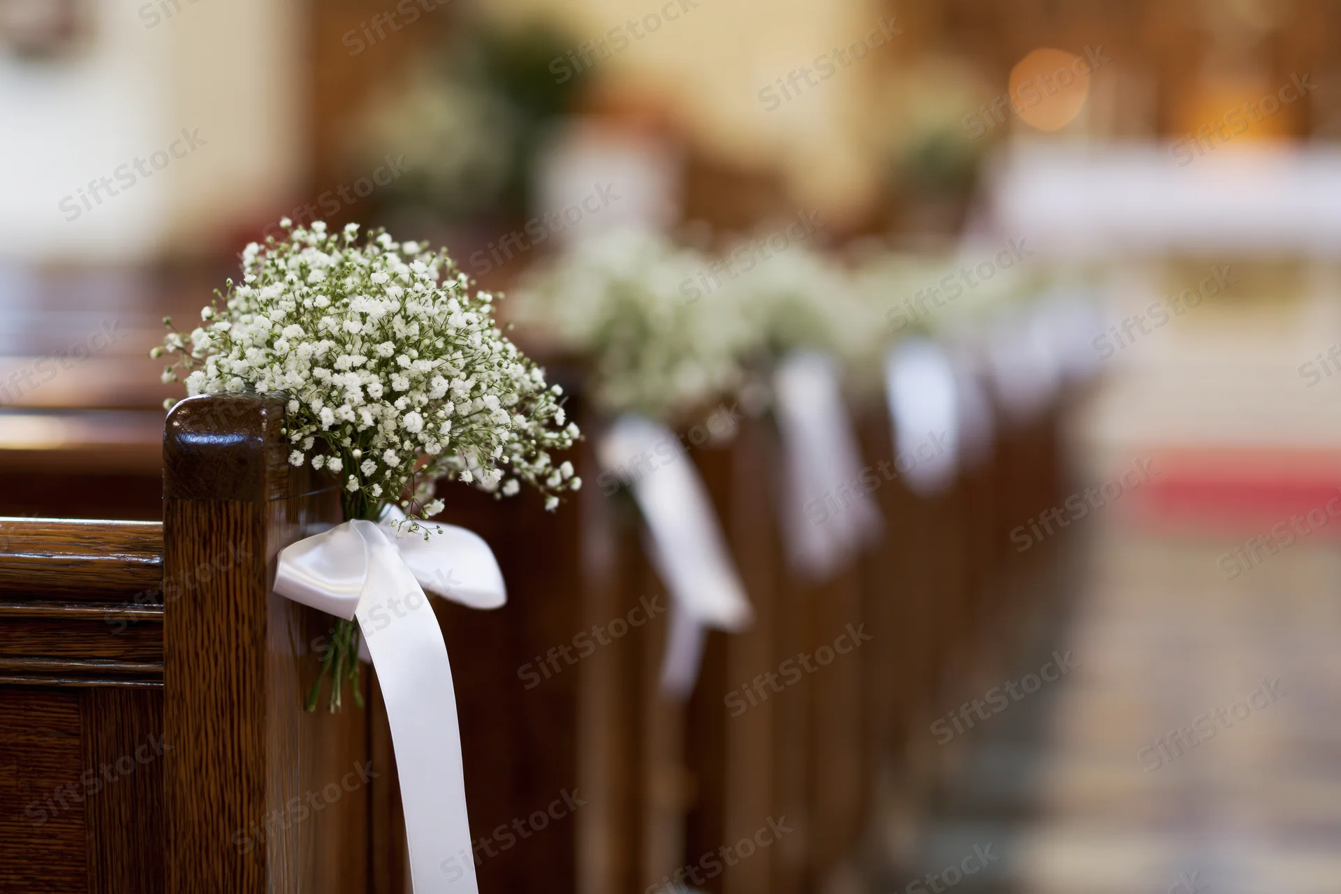 Baby's-breath flowers tied with white ribbons on dark wooden church pews lining an aisle