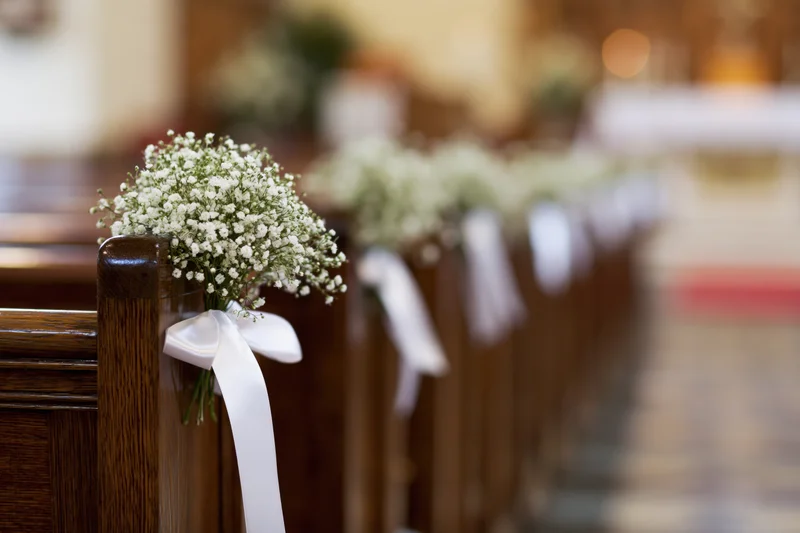 Baby's-breath flowers tied with white ribbons on dark wooden church pews lining an aisle