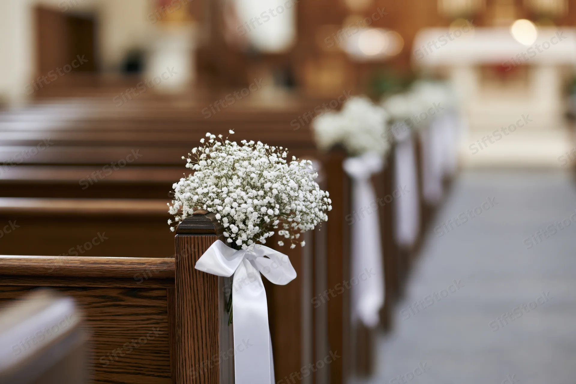 Baby's-breath flowers tied with white ribbon on wooden church pews lining the aisle
