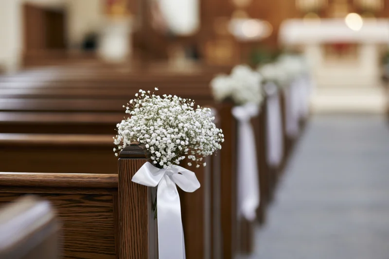Baby's-breath flowers tied with white ribbon on wooden church pews lining the aisle