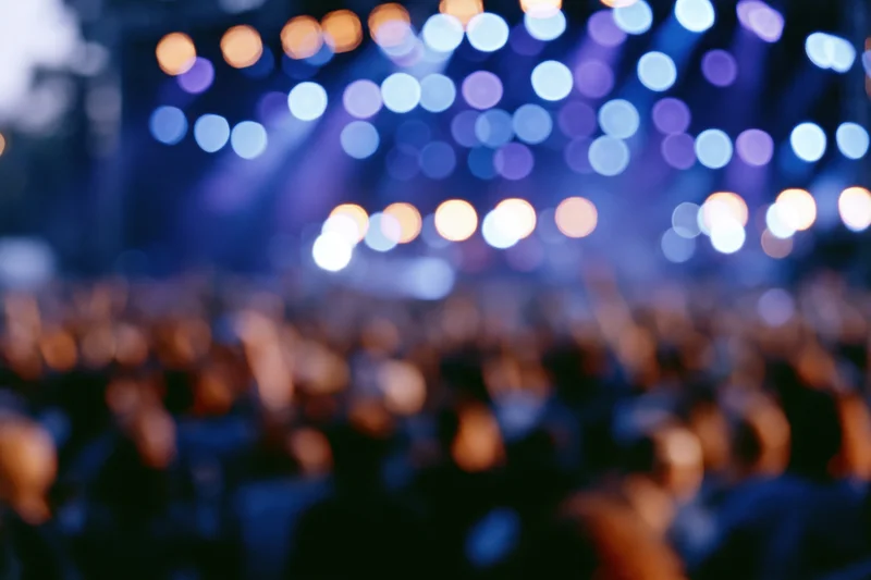 Blurred crowd silhouetted against a stage with colorful bokeh lights at a live music concert