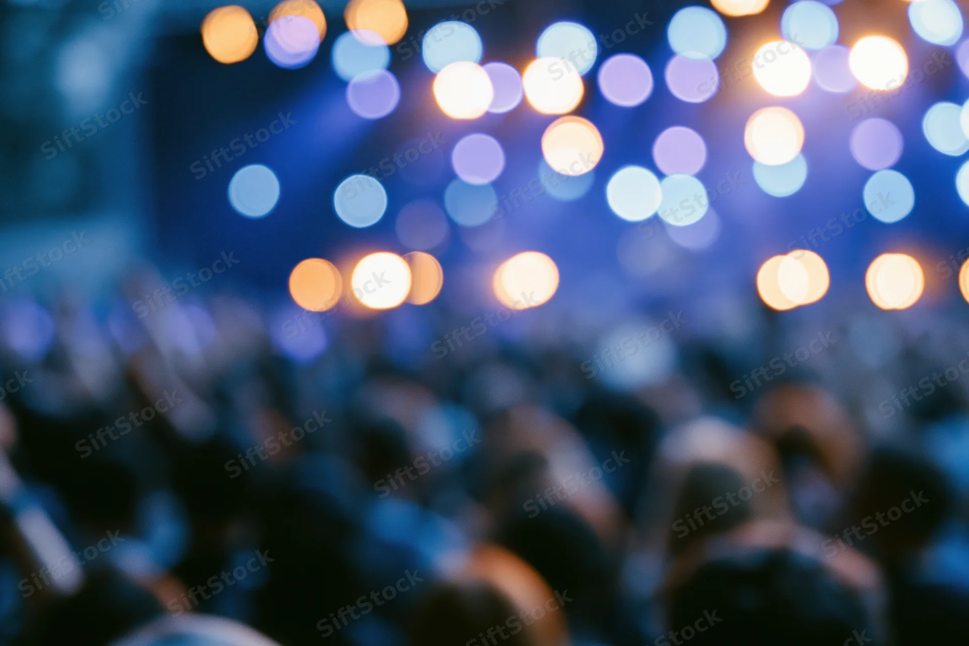 Defocused crowd silhouetted against stage lights at a live music concert