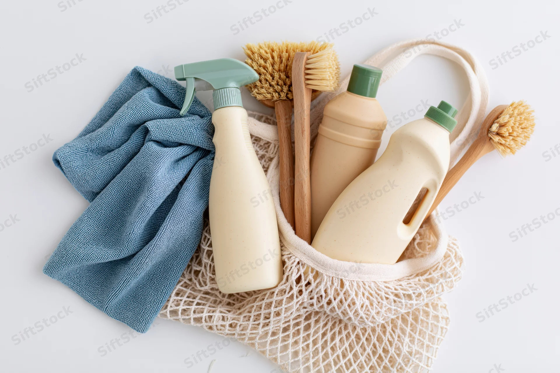 Eco-friendly cleaning supplies arranged in a white mesh bag with cloth and brushes on white background