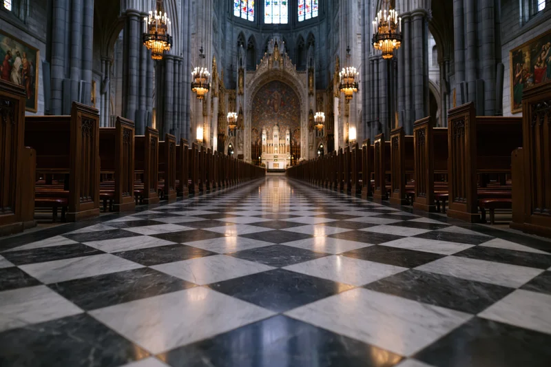 Central view of gothic cathedral interior with checkered marble floor and wooden pews leading to altar