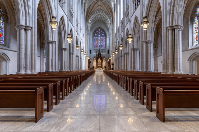 Empty gothic revival cathedral nave with wooden pews and stained glass windows along central aisle