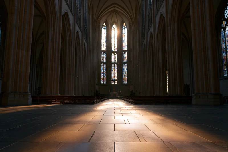 Interior of gothic cathedral with sunlight streaming through stained glass windows onto stone floor toward altar