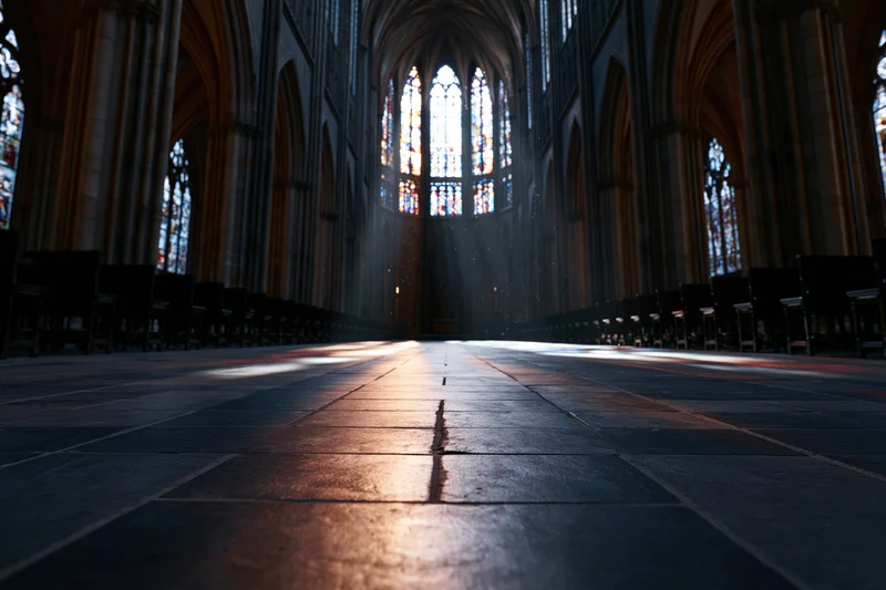 Low-angle view of empty gothic cathedral nave with sunlight streaming through stained glass toward the altar