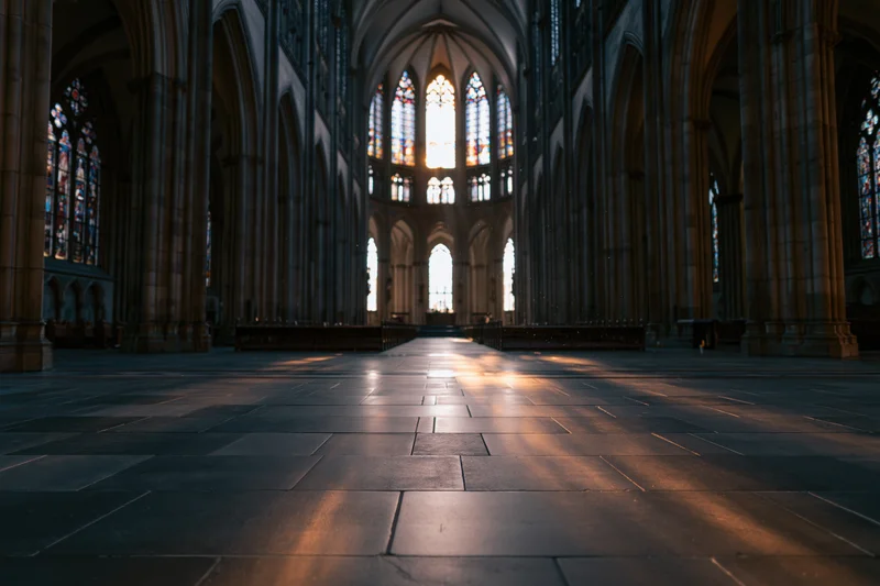 Empty gothic cathedral interior with sunlight streaming through stained glass windows toward the altar