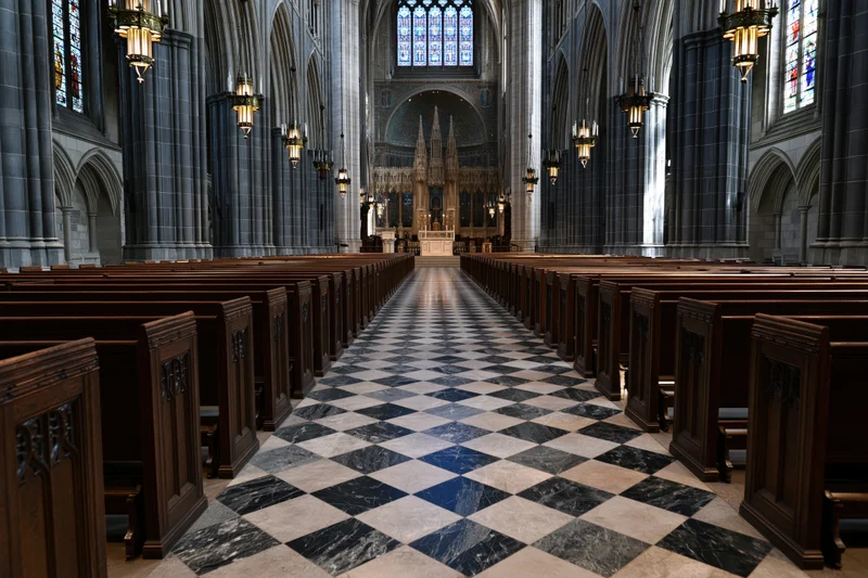 Gothic cathedral nave with wooden pews and checkered marble floor leading to altar