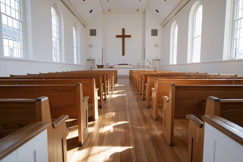 Empty protestant church interior with wooden pews and cross at the front, sunlight streaming through arched windows