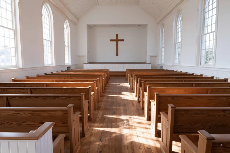 Empty protestant church interior with wooden pews and cross at altar, sunlight streaming through arched windows