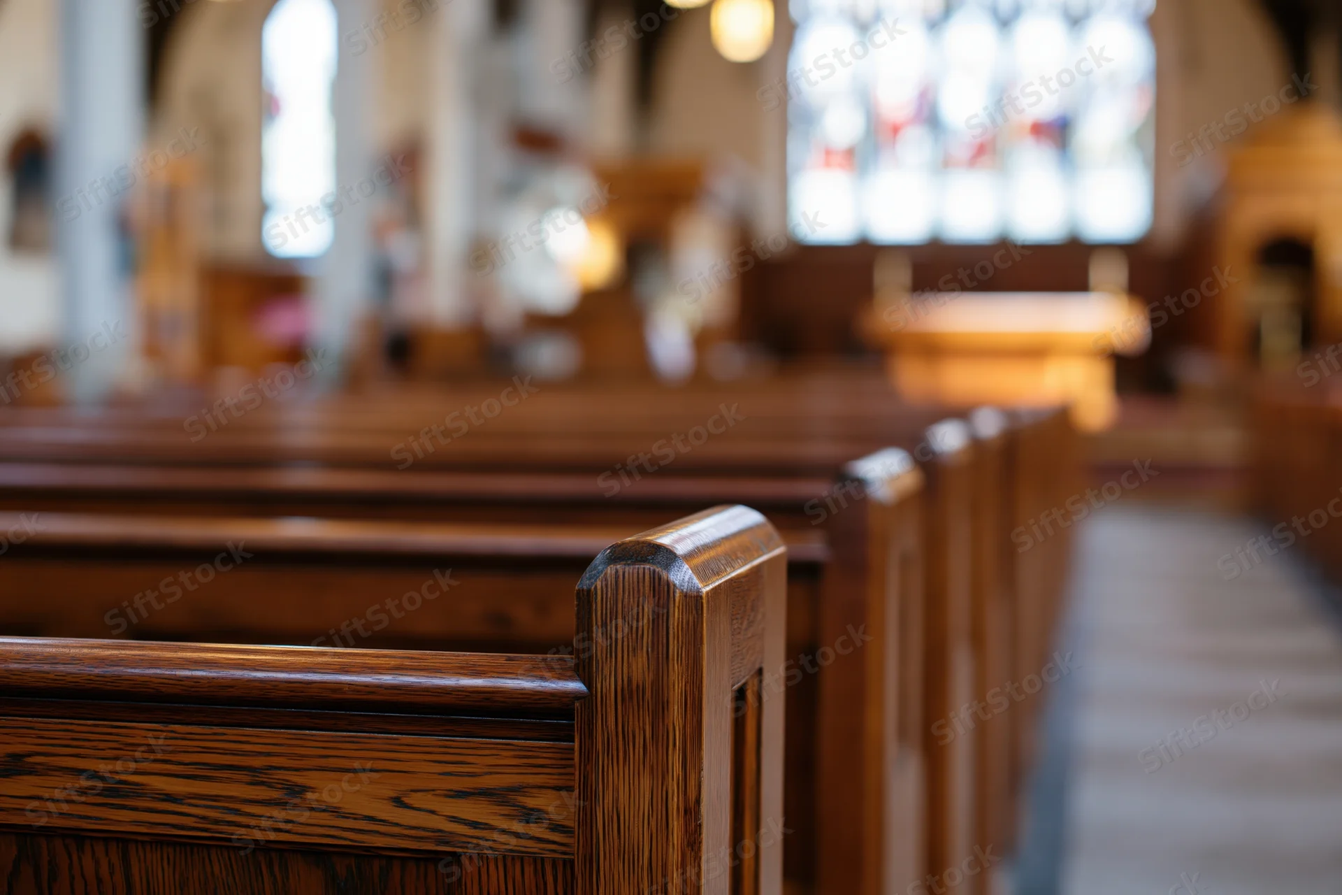 Wooden pews lining the central aisle in a church interior with stained glass windows in the background