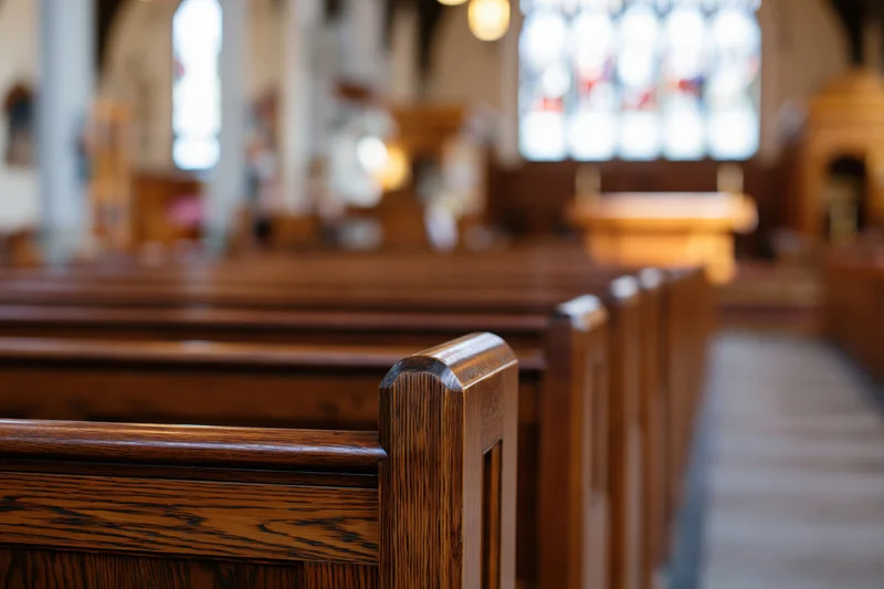Wooden pews lining the central aisle in a church interior with stained glass windows in the background