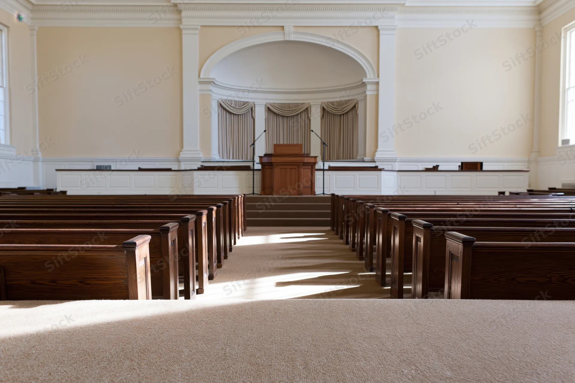Empty church interior viewed from center aisle with wooden pews leading to pulpit under natural light