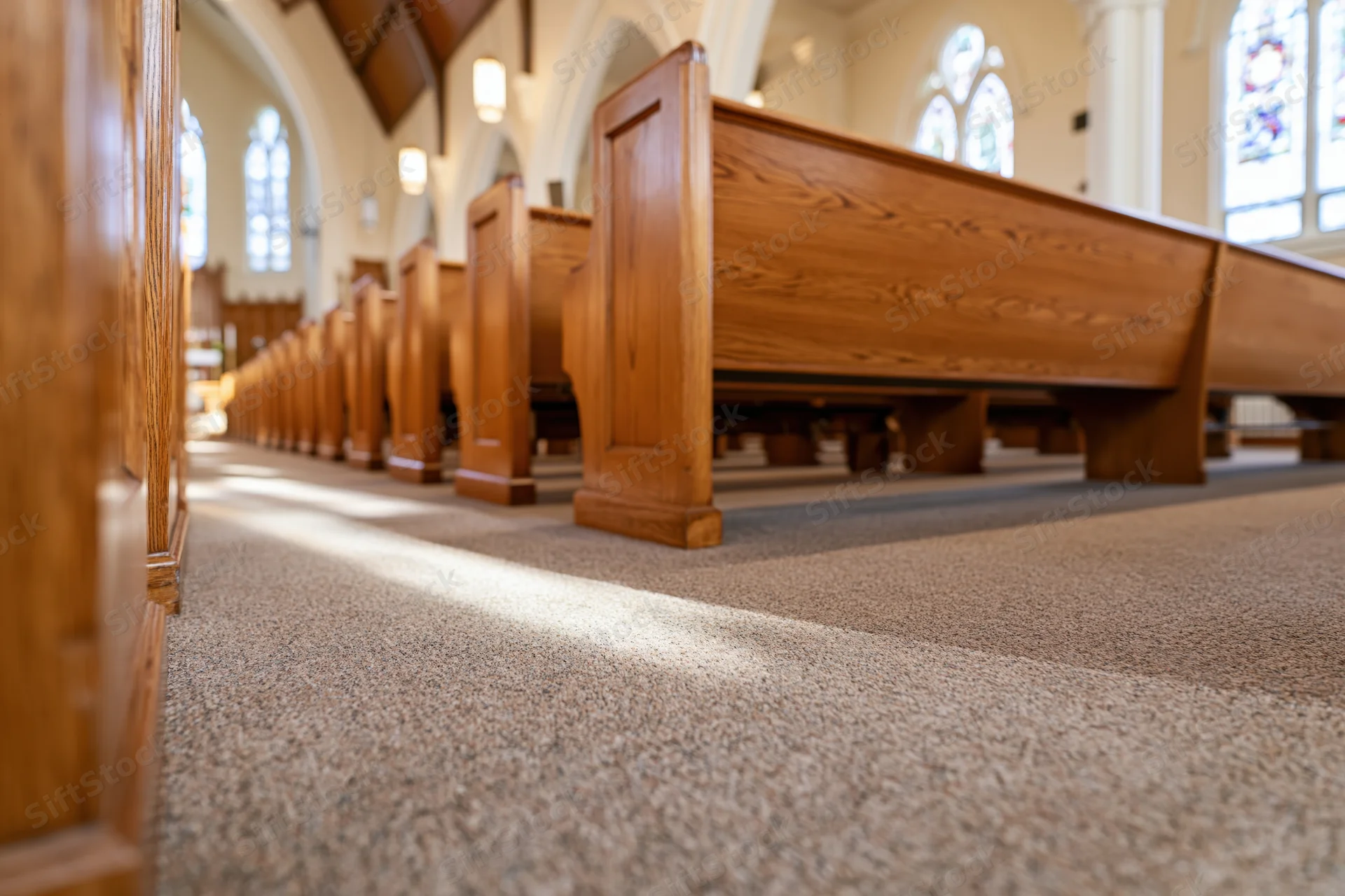 Rows of polished wooden pews in a church interior with sunlight streaming through stained glass windows