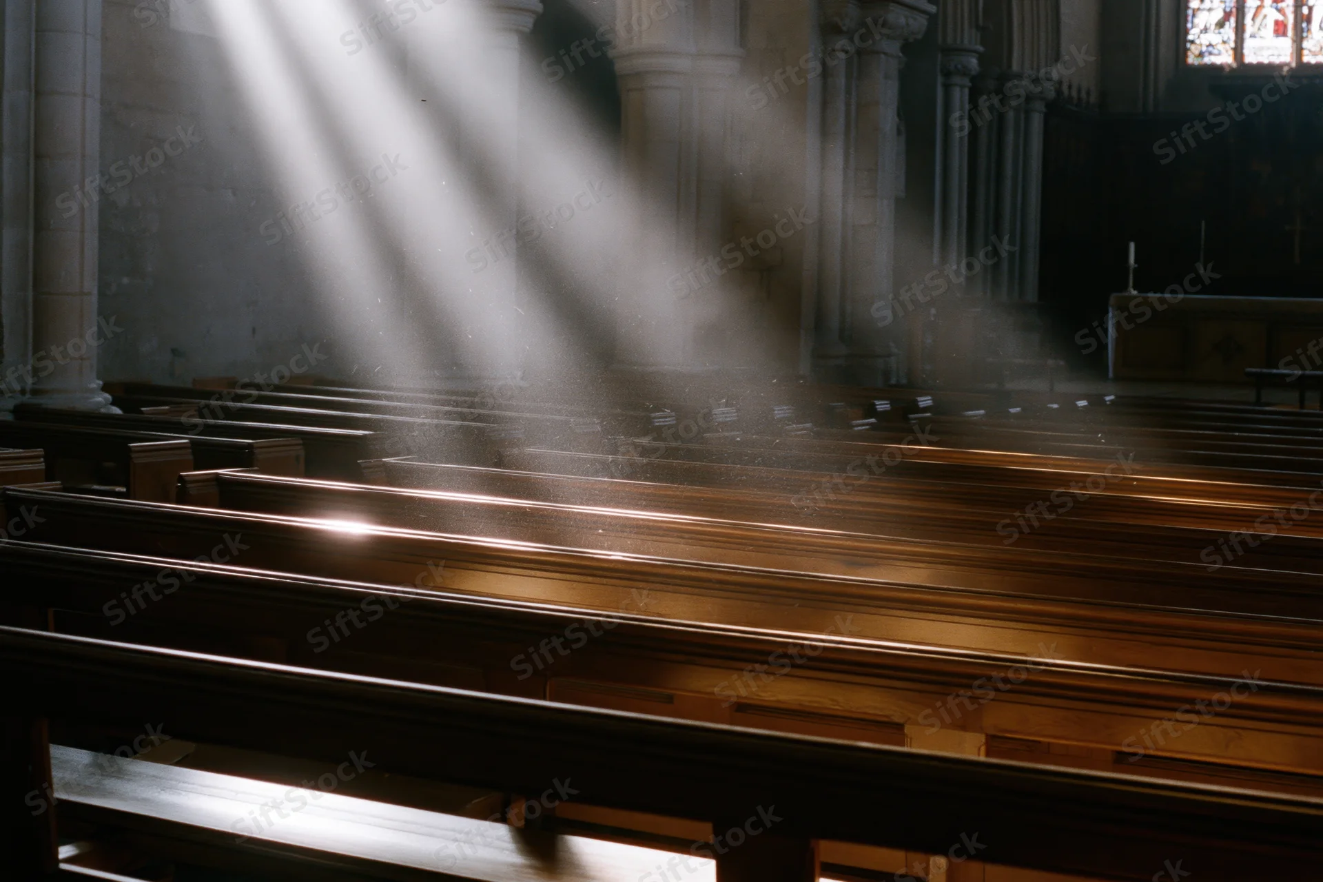 Rows of wooden pews in a church interior illuminated by sunlight beams through stained glass windows