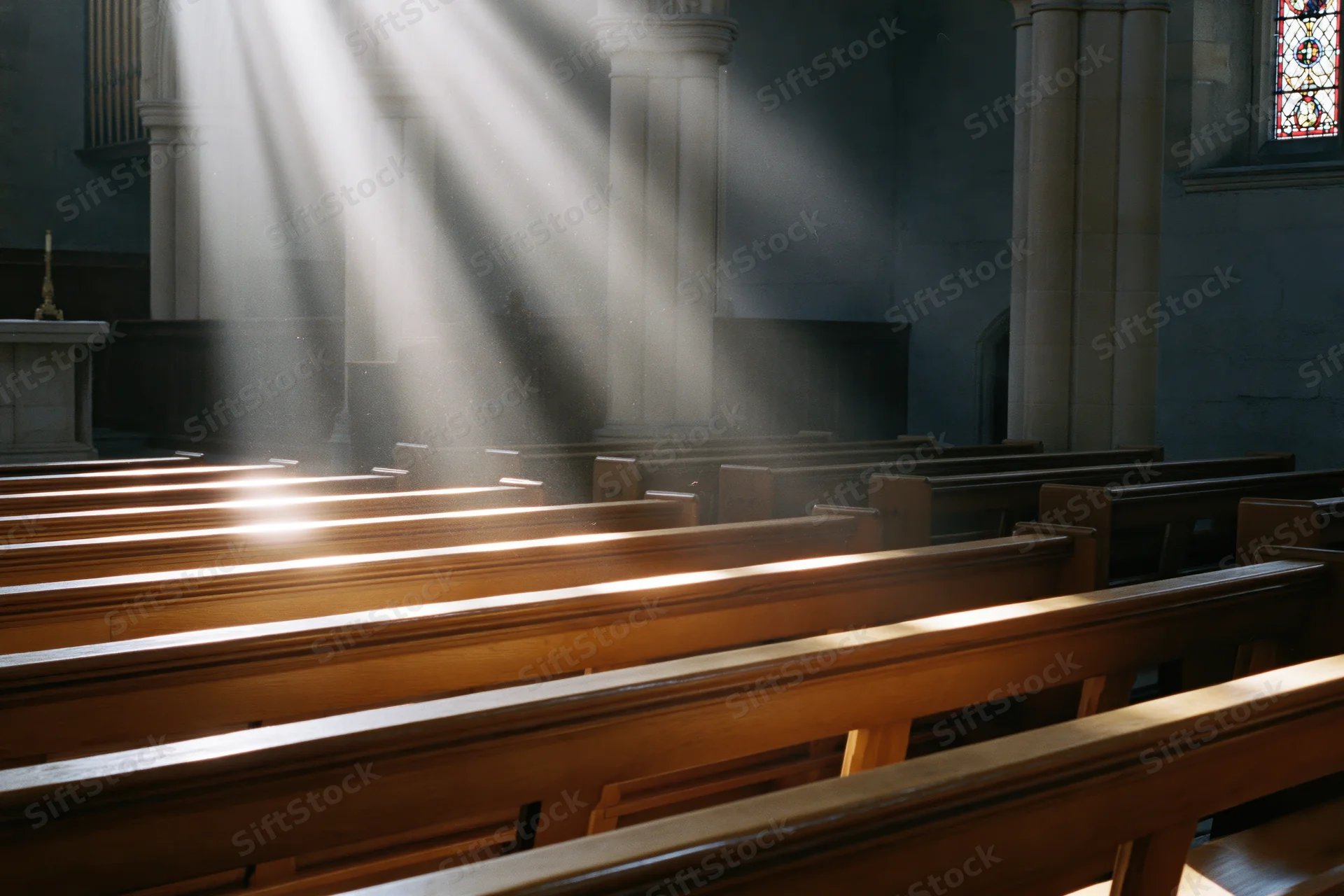 Rows of wooden pews in a church interior illuminated by sunlight streaming through stained glass windows