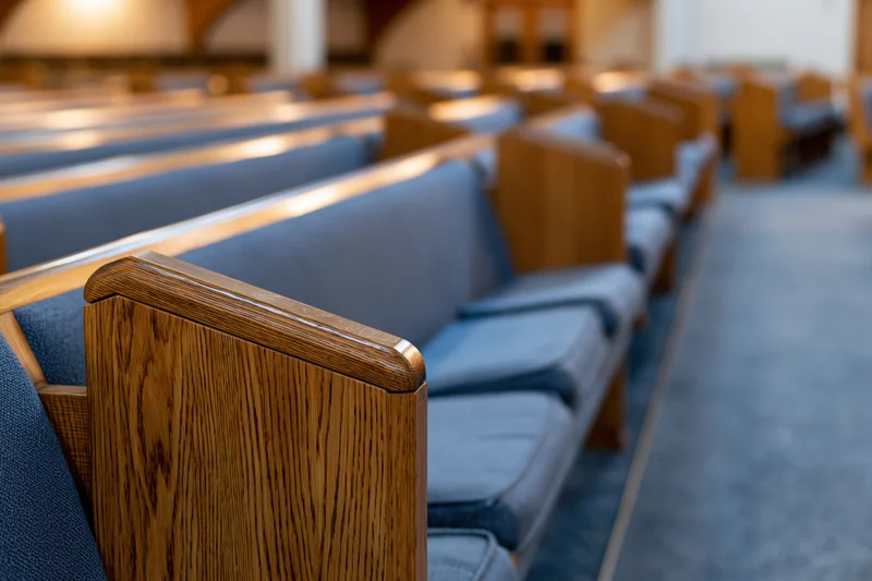 Rows of wooden church pews with blue cushions receding in perspective along the aisle