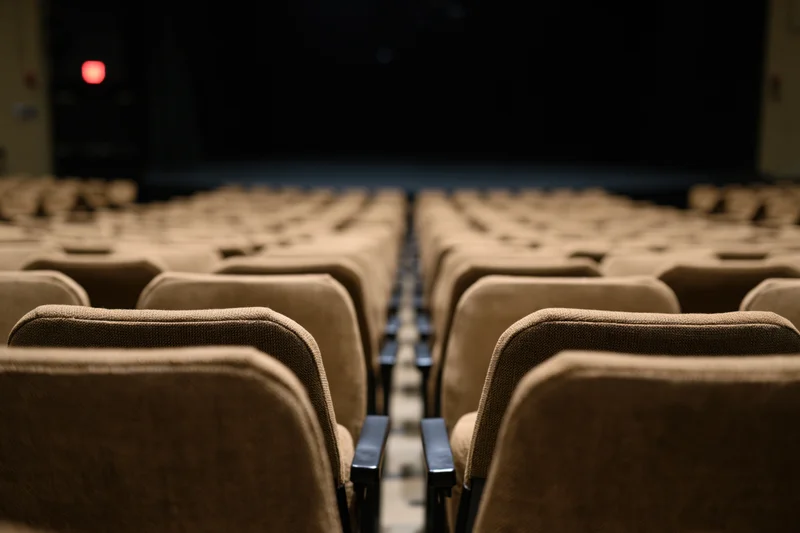 Rows of empty upholstered theater seats stretching toward a dark stage in an auditorium