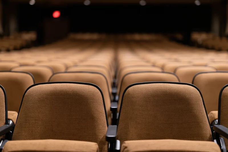 Empty rows of upholstered theater seats stretching toward a dark stage