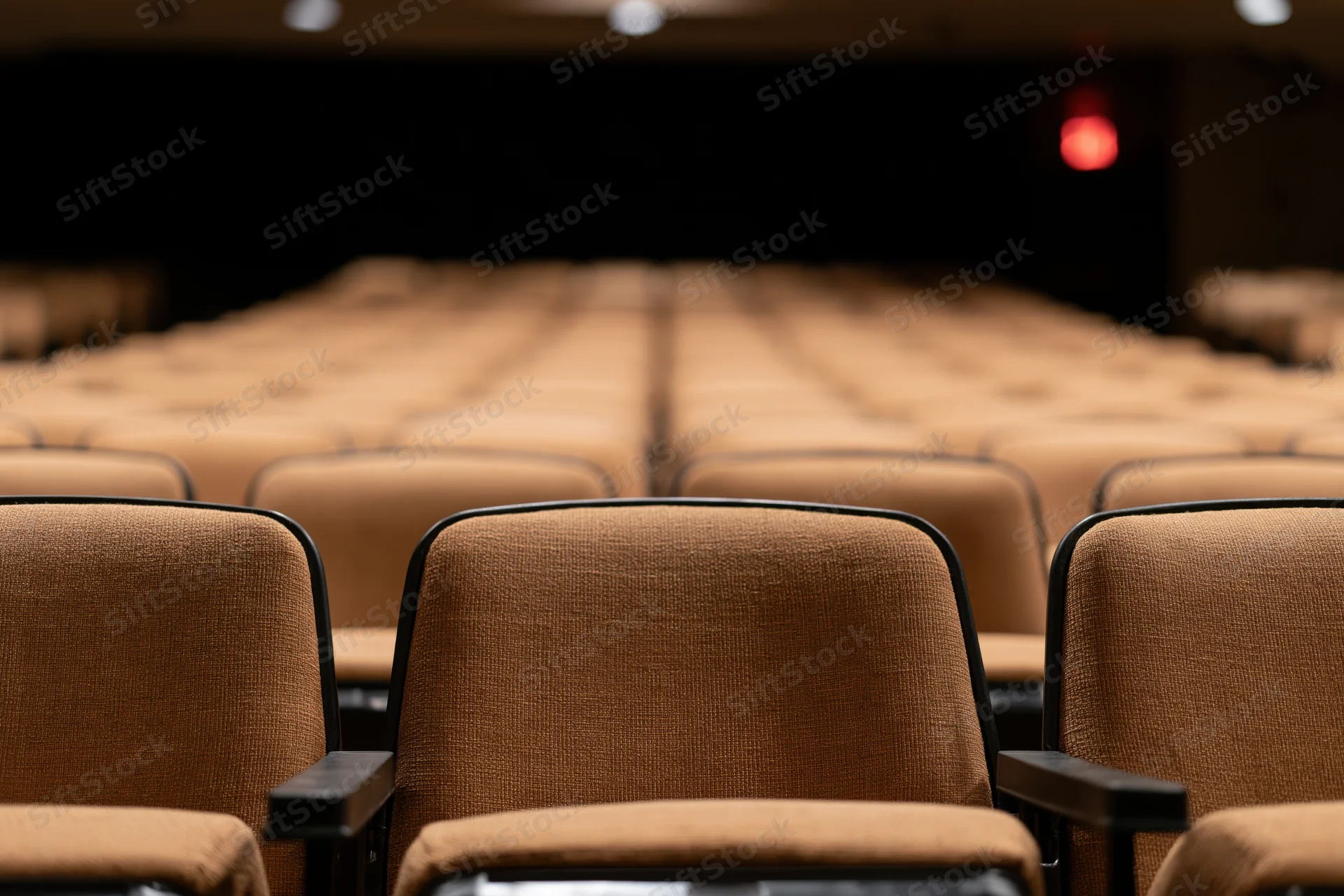 Empty rows of brown upholstered theater seats stretching toward a dark stage