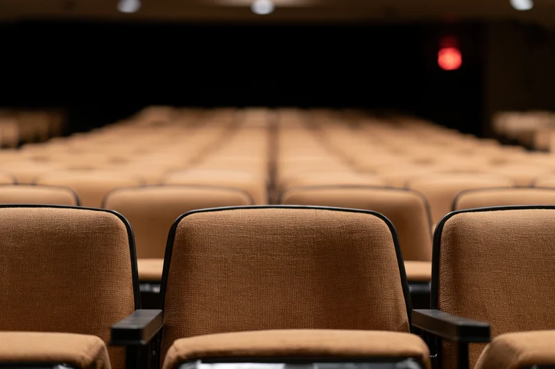Empty rows of brown upholstered theater seats stretching toward a dark stage