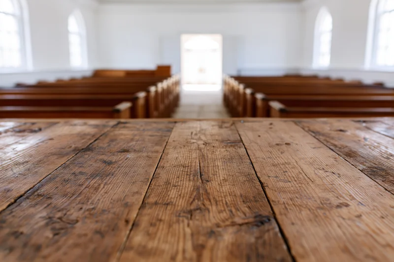 Wooden table in foreground of empty church interior with pews and arched windows
