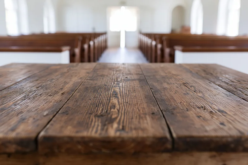 Weathered wooden table in foreground of church interior with pews and altar in soft focus background