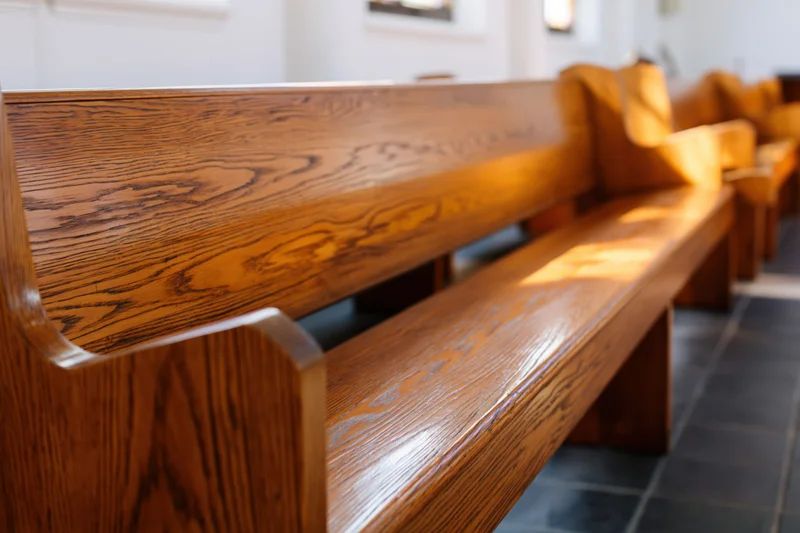 Wooden church pews in a row inside a sanctuary with sunlight streaming through windows