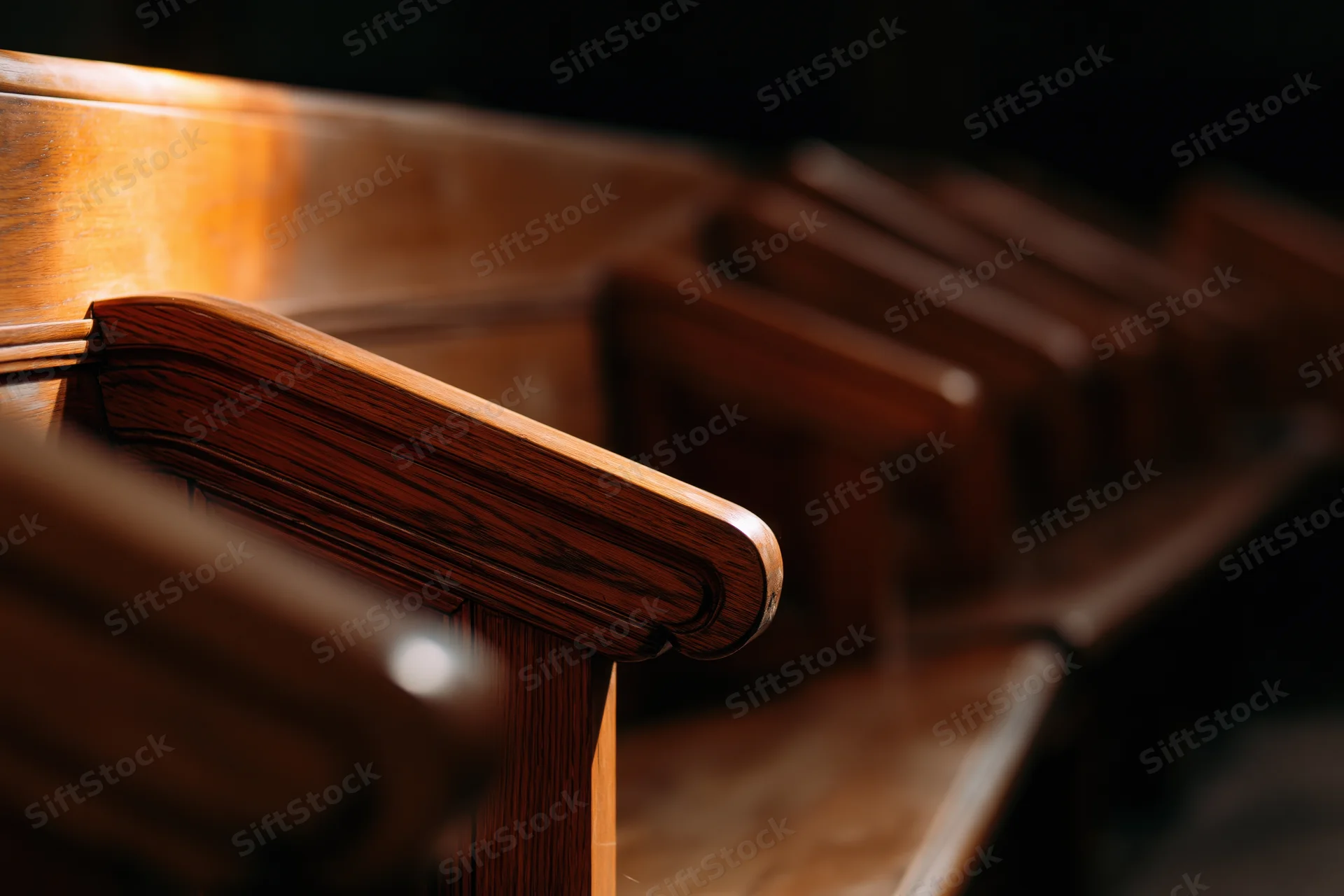 Wooden church pews receding into shadowed interior with warm light on polished grain