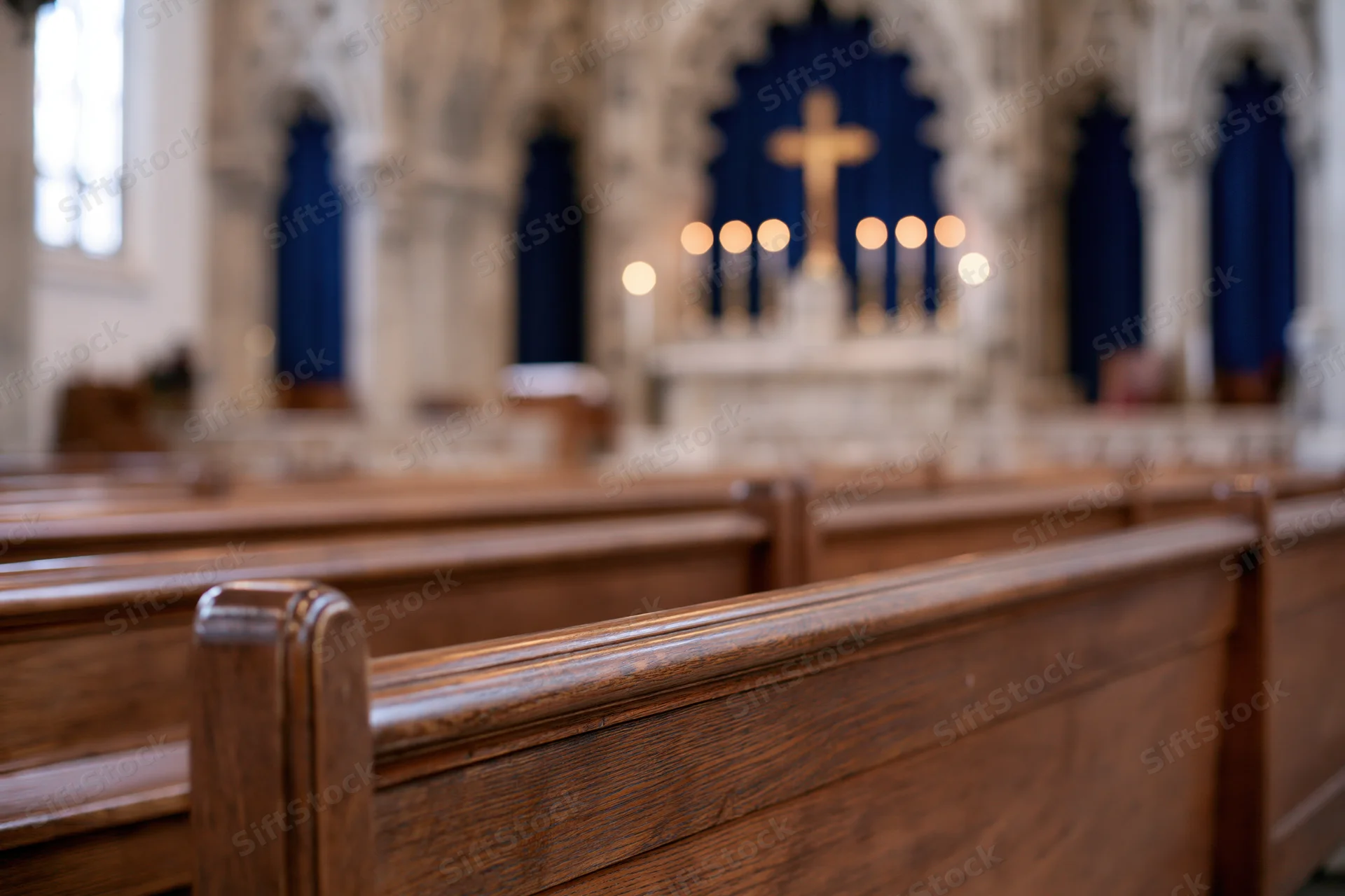 Wooden church pews receding toward an ornate altar with a golden cross and lit candles in a gothic sanctuary