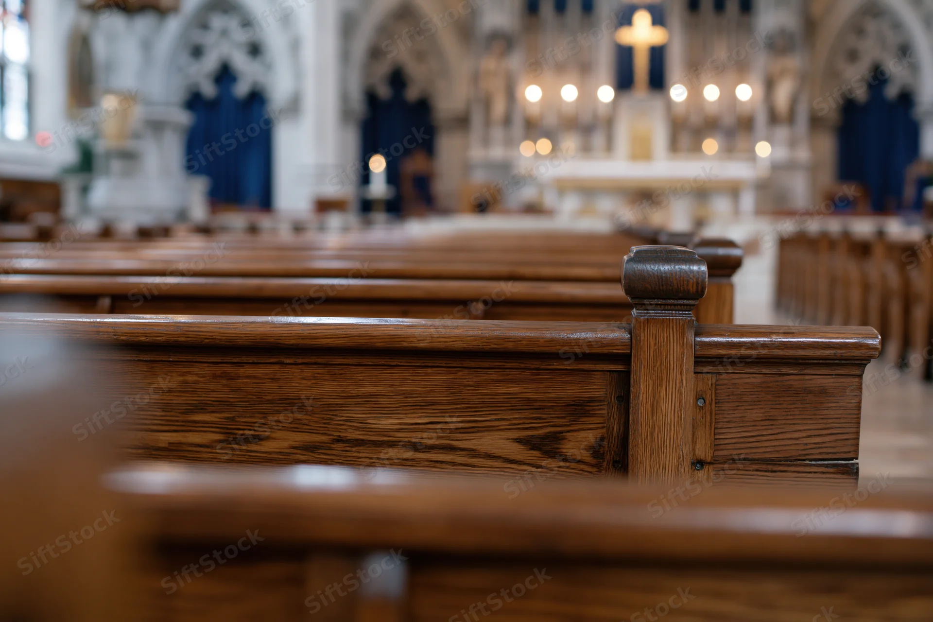 Wooden church pews receding toward altar with cross and candles in sanctuary