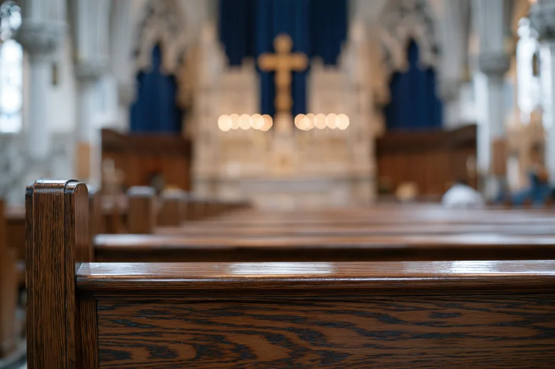 Wooden church pews receding toward an altar with a cross and candles in a gothic interior