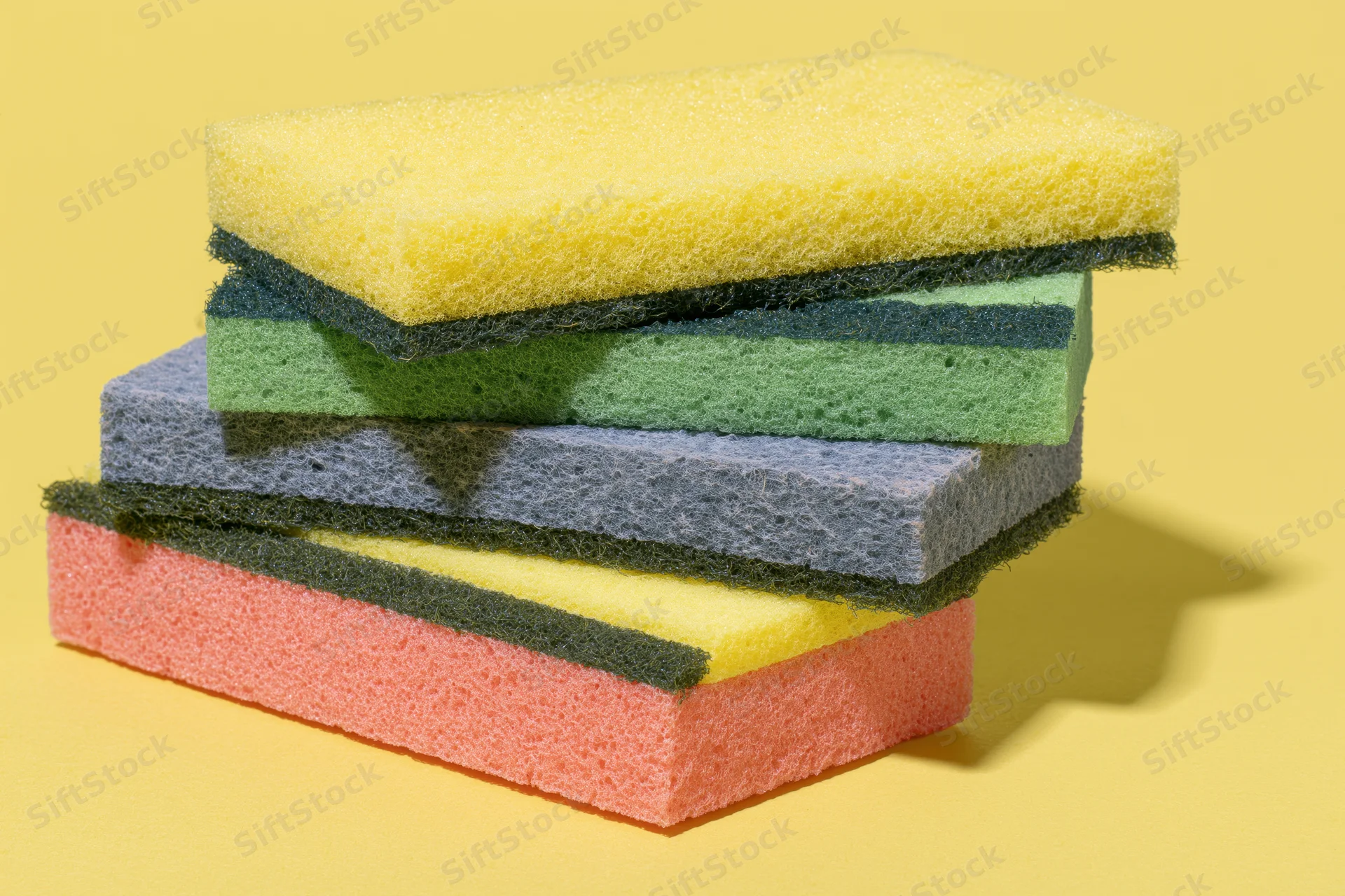 Stack of colorful rectangular kitchen sponges arranged in alternating layers on a yellow surface