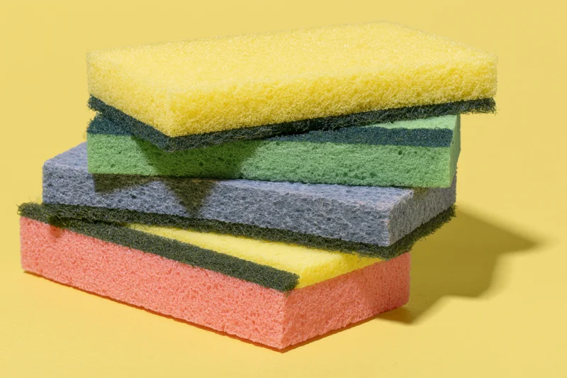 Stack of colorful rectangular kitchen sponges arranged in alternating layers on a yellow surface