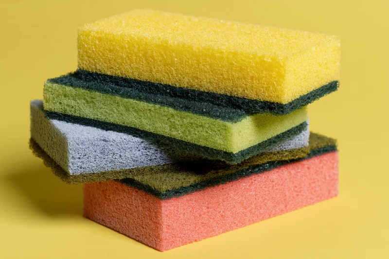 Stack of colorful rectangular kitchen sponges arranged in alternating layers on a yellow background