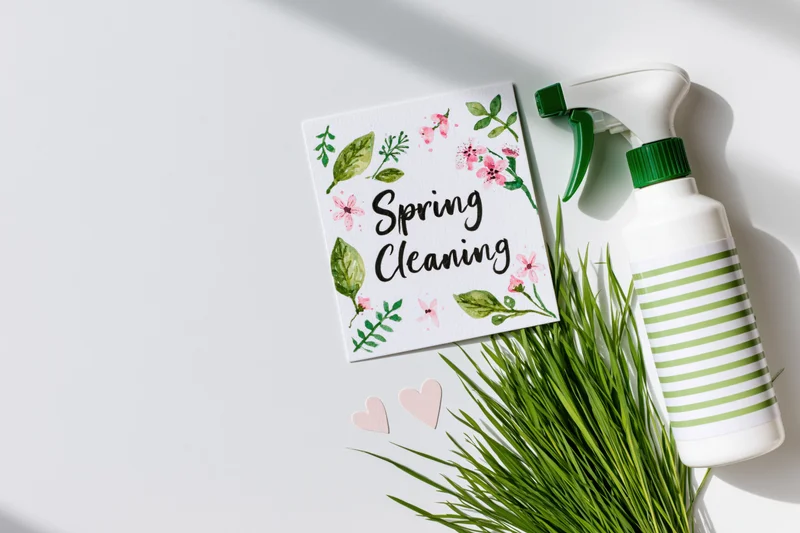 Spring cleaning card with floral design and spray bottle on white surface with green grass and paper hearts