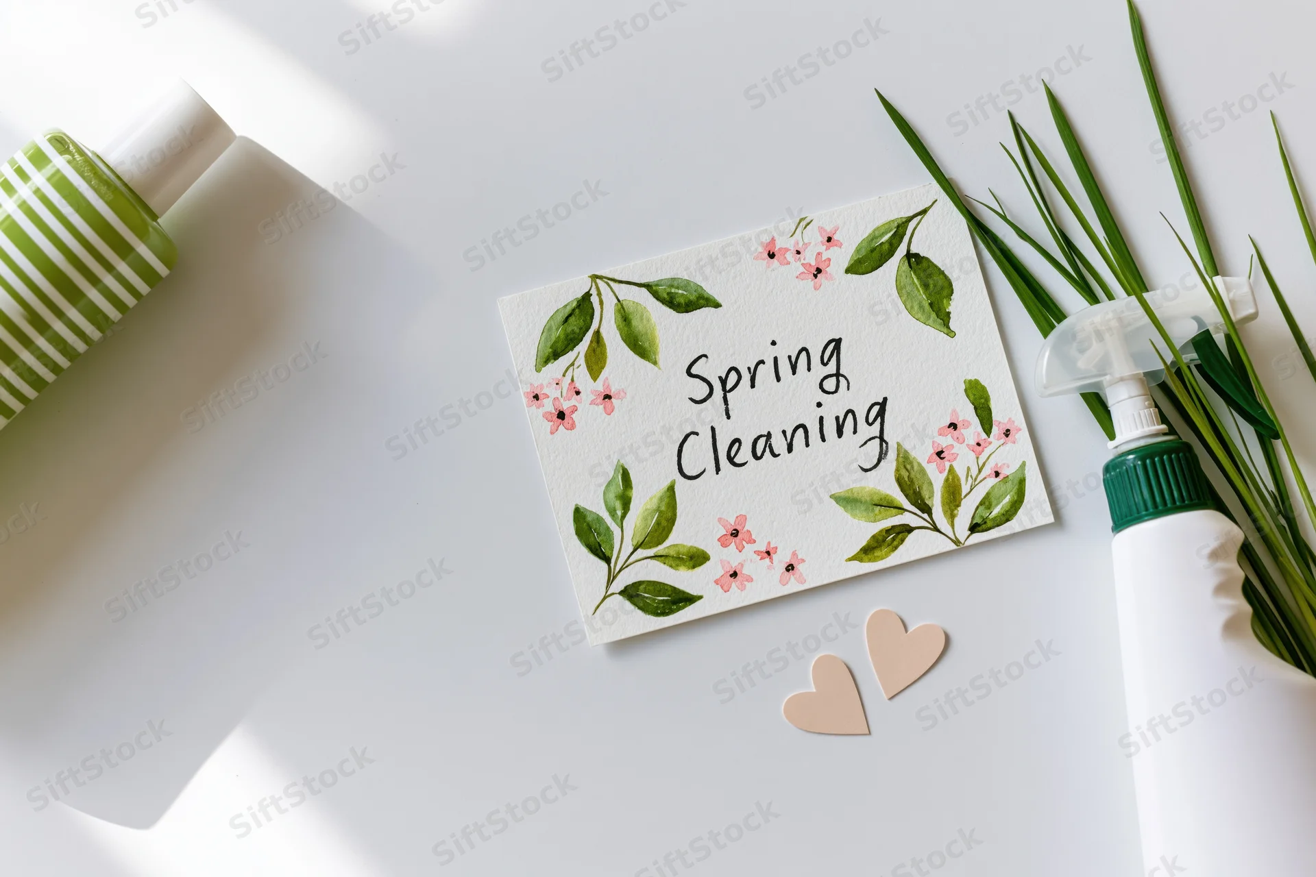 Handwritten spring cleaning card with floral decoration on white surface surrounded by cleaning bottles and greenery
