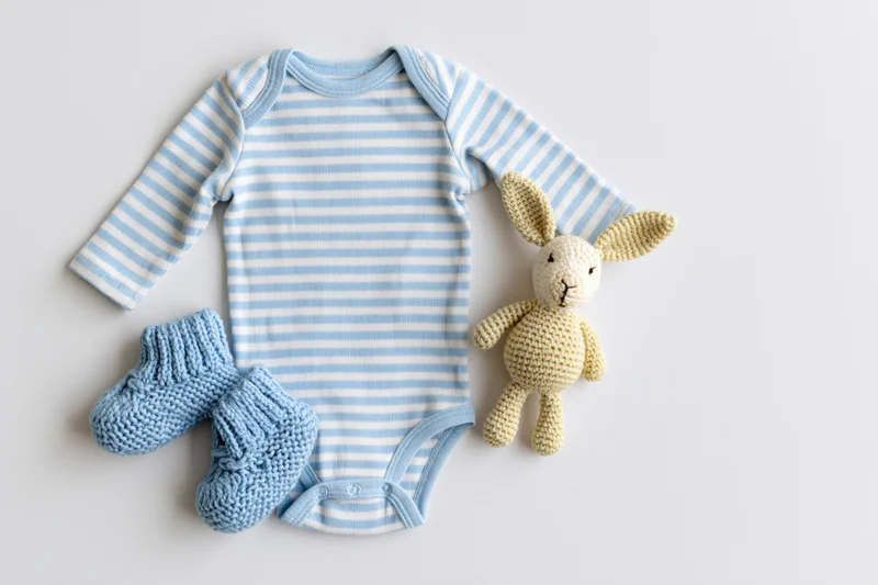 Baby onesie with matching knitted socks and crocheted bunny toy arranged flat on white surface