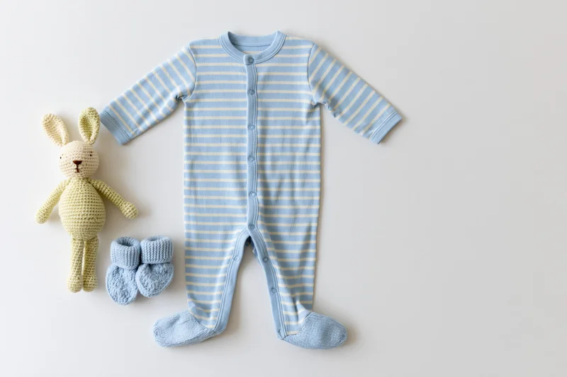 Baby onesie with matching booties and crocheted bunny toy arranged in flat lay on white surface