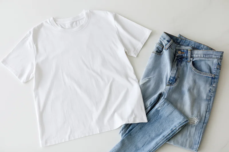 White cotton t-shirt and blue jeans laid flat on white surface